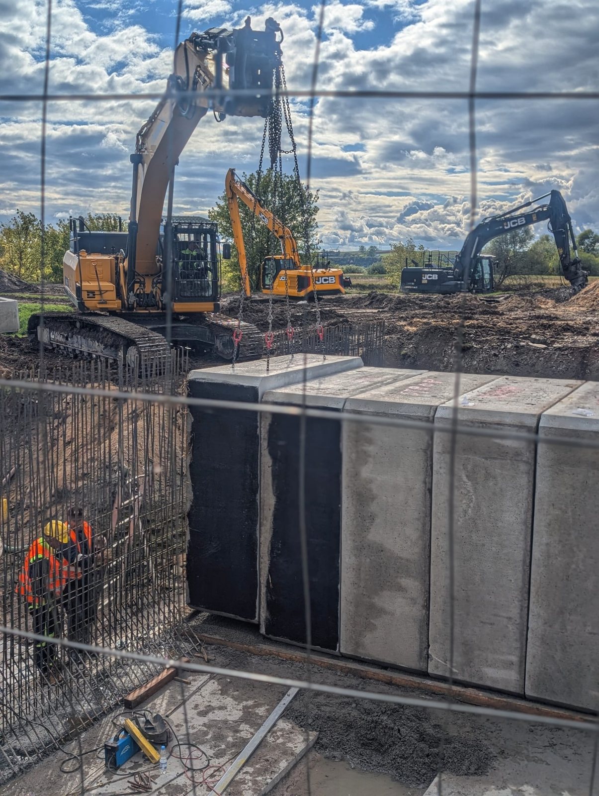 Montaż prefabrykowanych elementów betonowych przy obiekcie hydrotechnicznym z użyciem koparek JCB